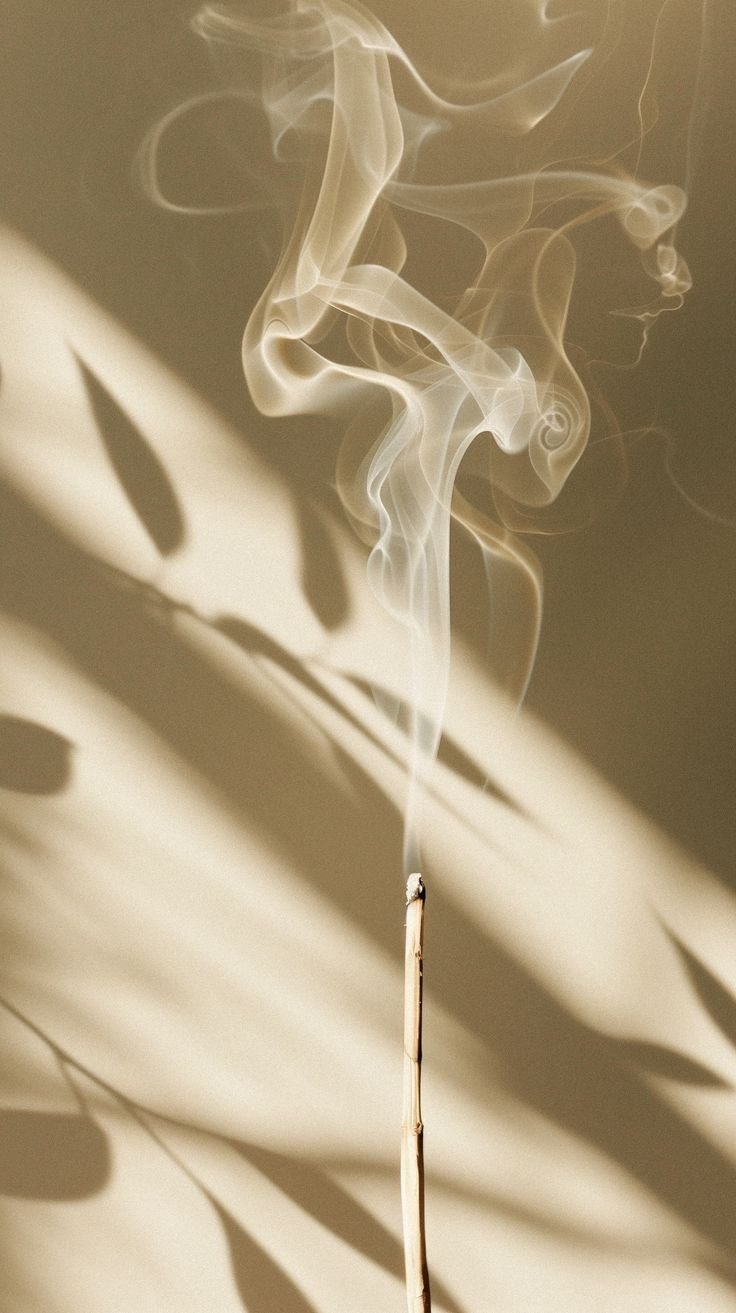 Close-up of a burning incense stick with white smoke forming intricate swirls and patterns.