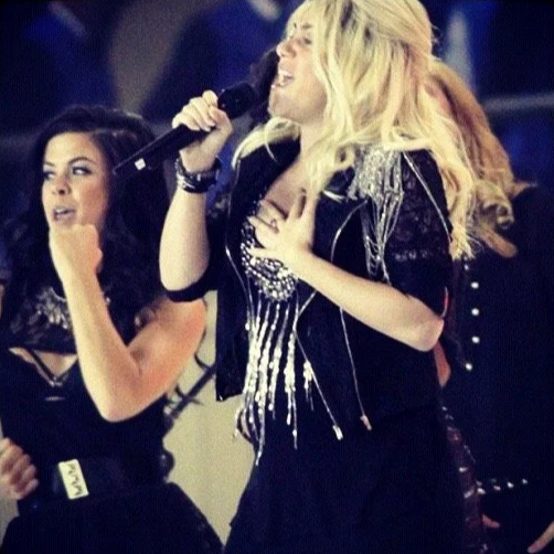 Women singing into microphones on stage at a concert or event.