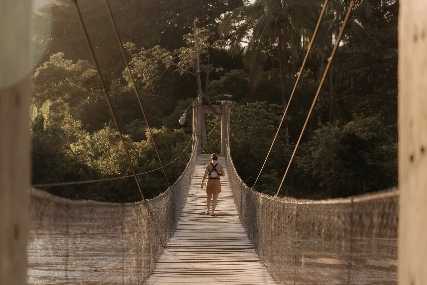 A woman walking across a suspension bridge in a forested area during daylight