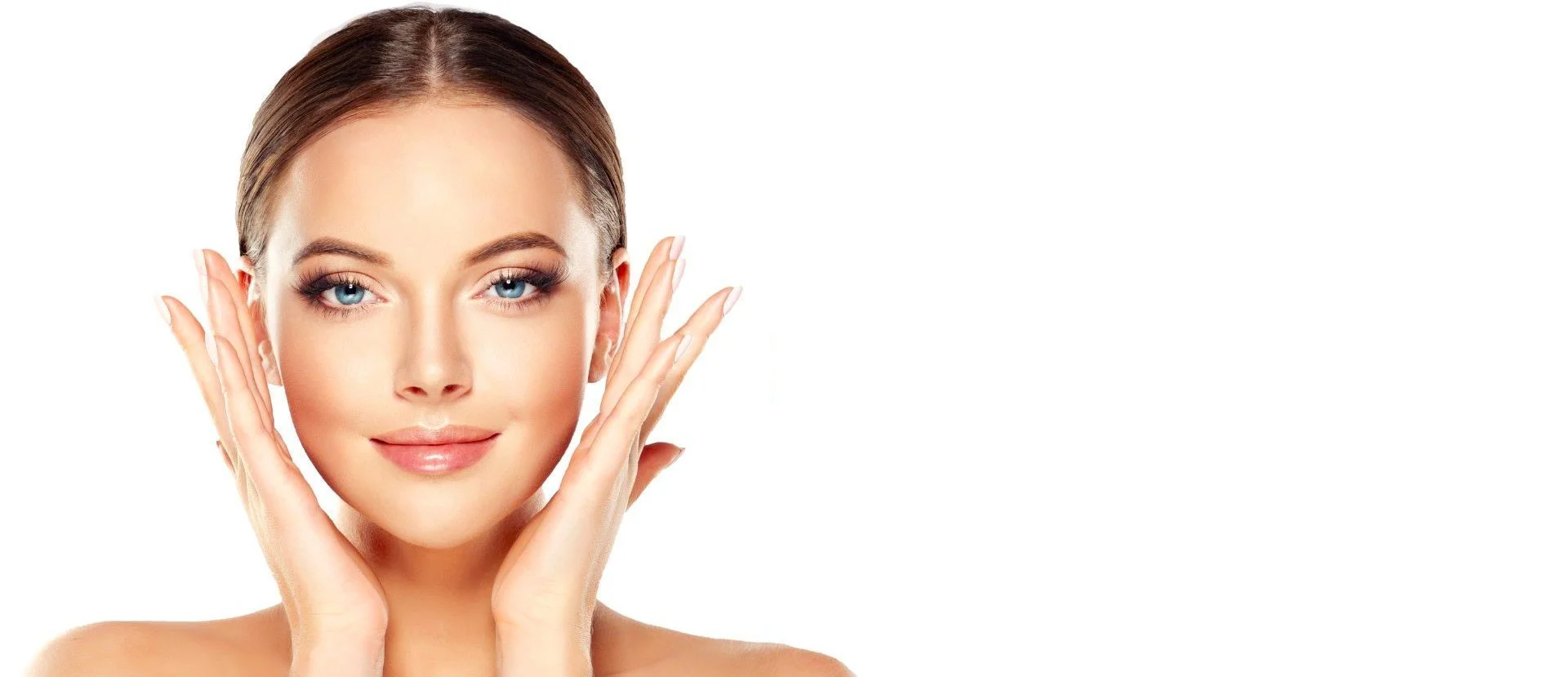 Close-up of a young woman with clear skin and blue eyes, gently holding her face with her hands, smiling softly, with a plain white background.