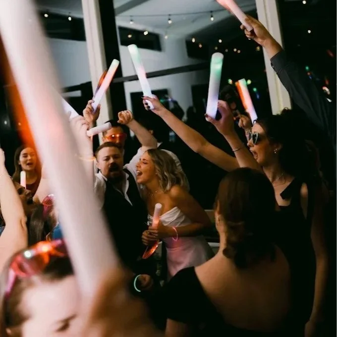 People celebrating at a party holding glowing sticks in a dimly lit indoor setting.