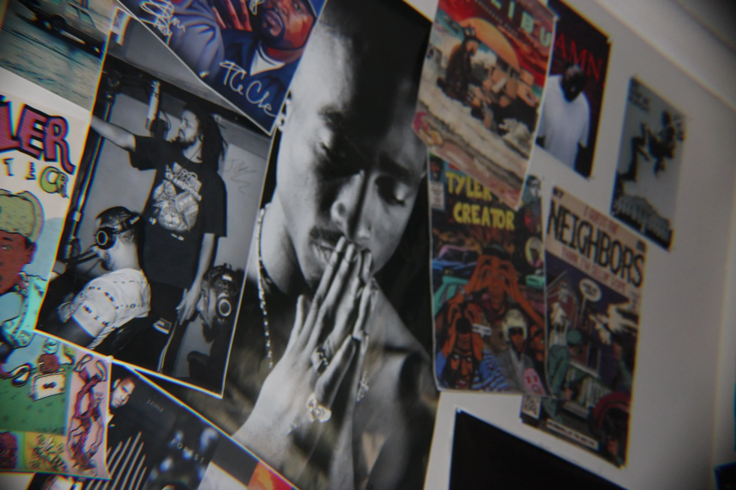 Collage of various posters and photos on a wall, including a black and white picture of a person with closed eyes, hands together, and praying, surrounded by colorful comic and art posters.