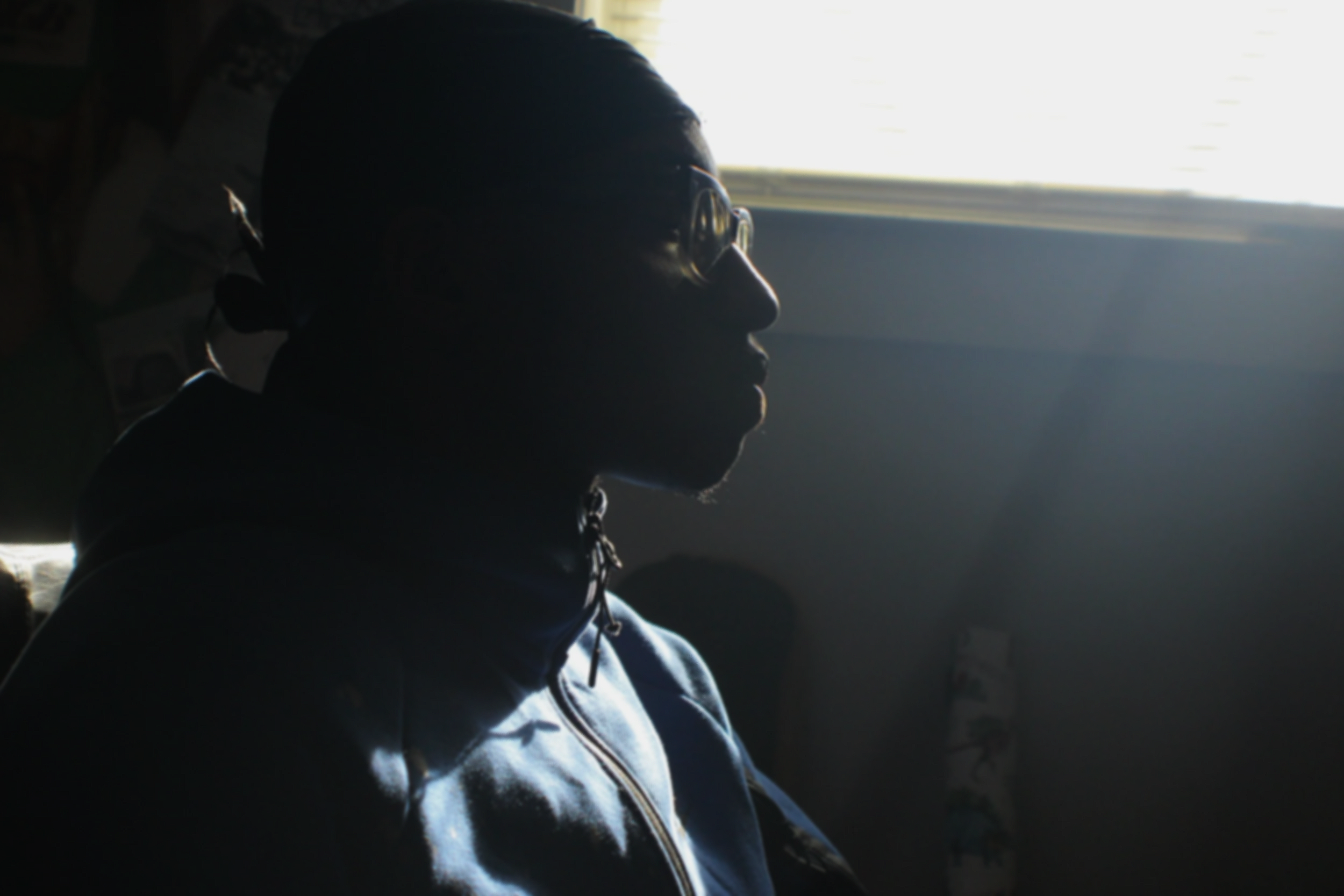 A person with glasses sitting indoors near a window, backlit by sunlight.