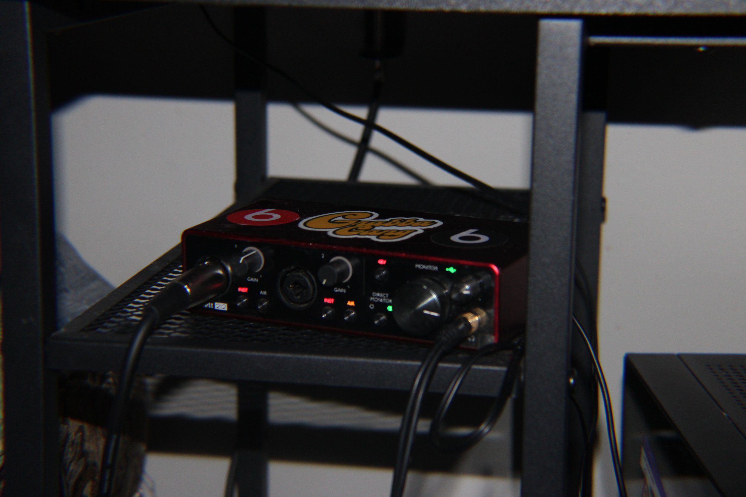 A black electronic device with various knobs and indicator lights, placed on a black shelf, connected by cables.