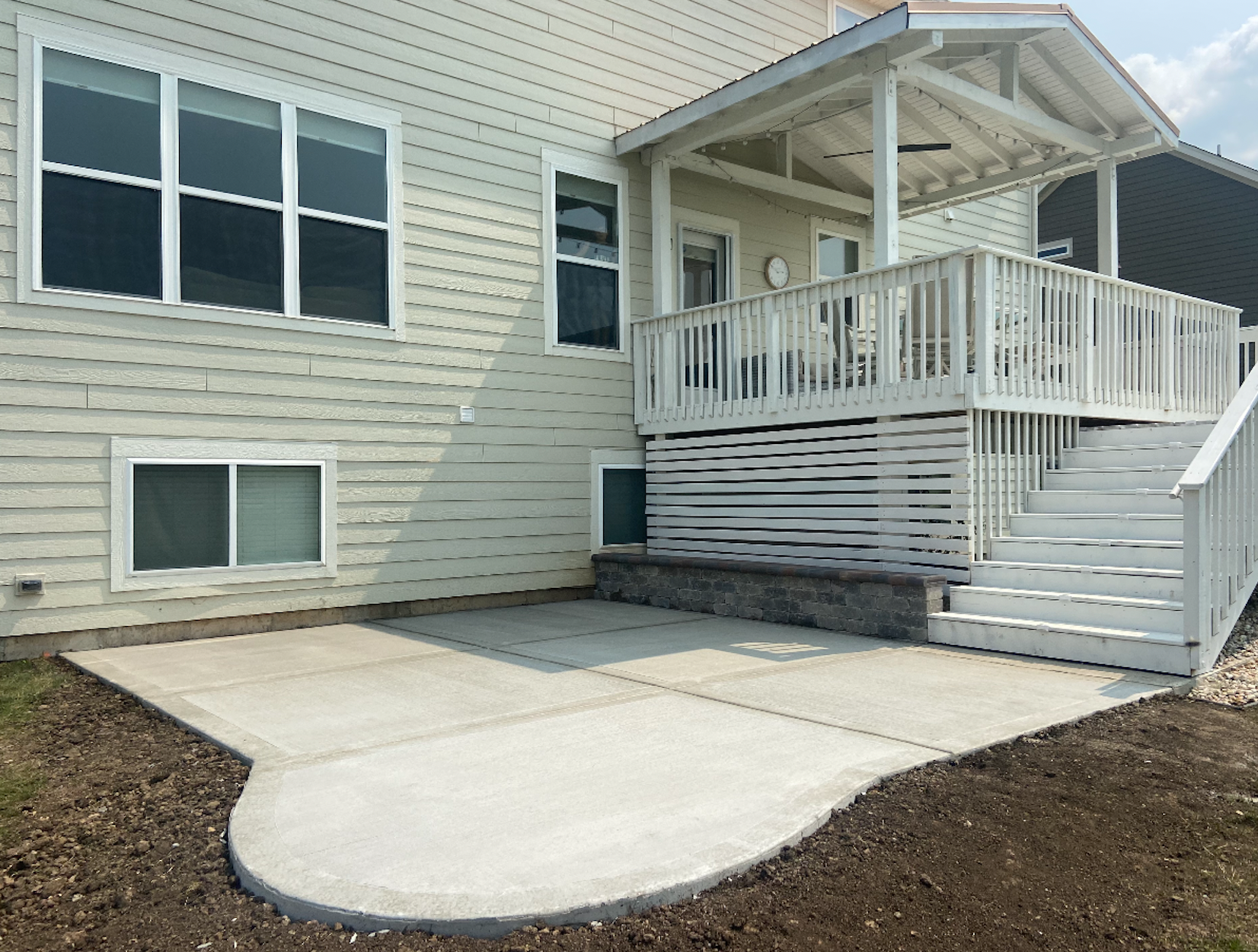 Backyard with a concrete patio, stairs leading up to a raised porch with white railing, and the house's beige siding with multiple windows.