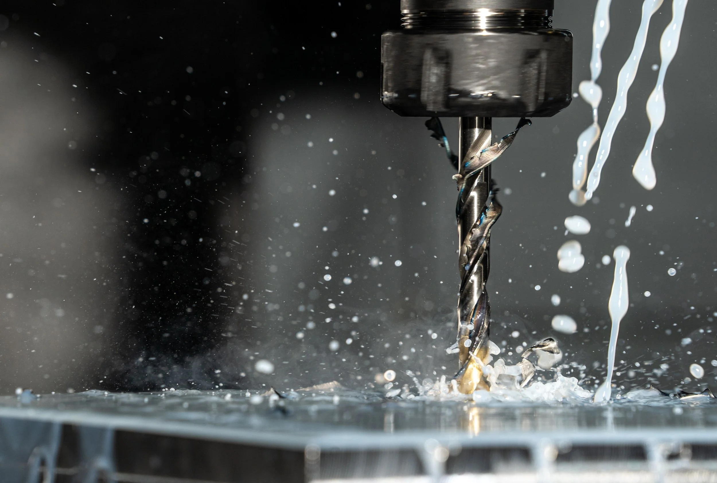 Close-up of a drill bit in a CNC machine with coolant spraying around it during machining.