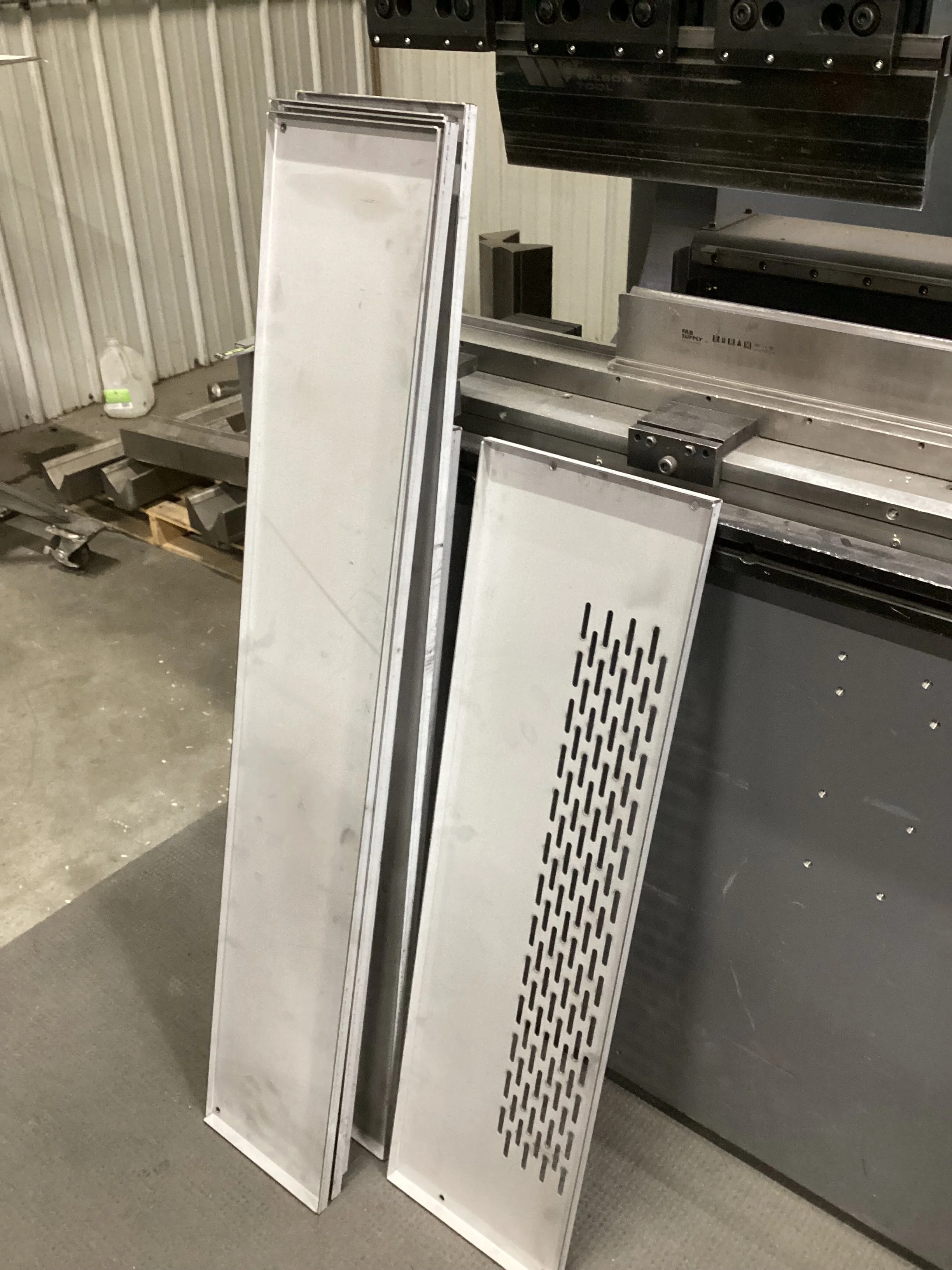 Metal sheets and panels leaning against a wall and a larger piece of equipment with a black top in a warehouse or industrial setting.