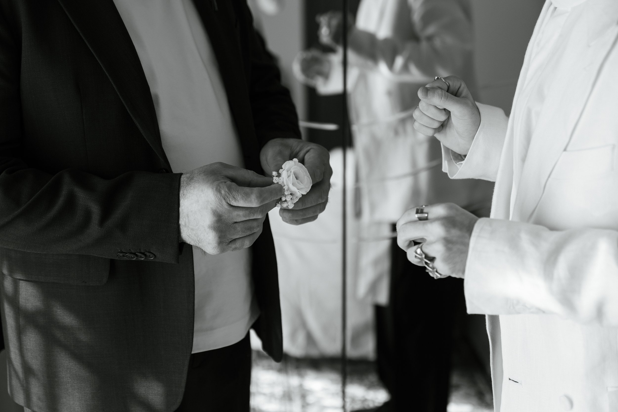 Due persone scambiano un due in un ambiente formale, uno indossa un abito nero e l'altro un completo bianco, l'attenzione è sui loro mani e sui dettagli delle loro scarpe