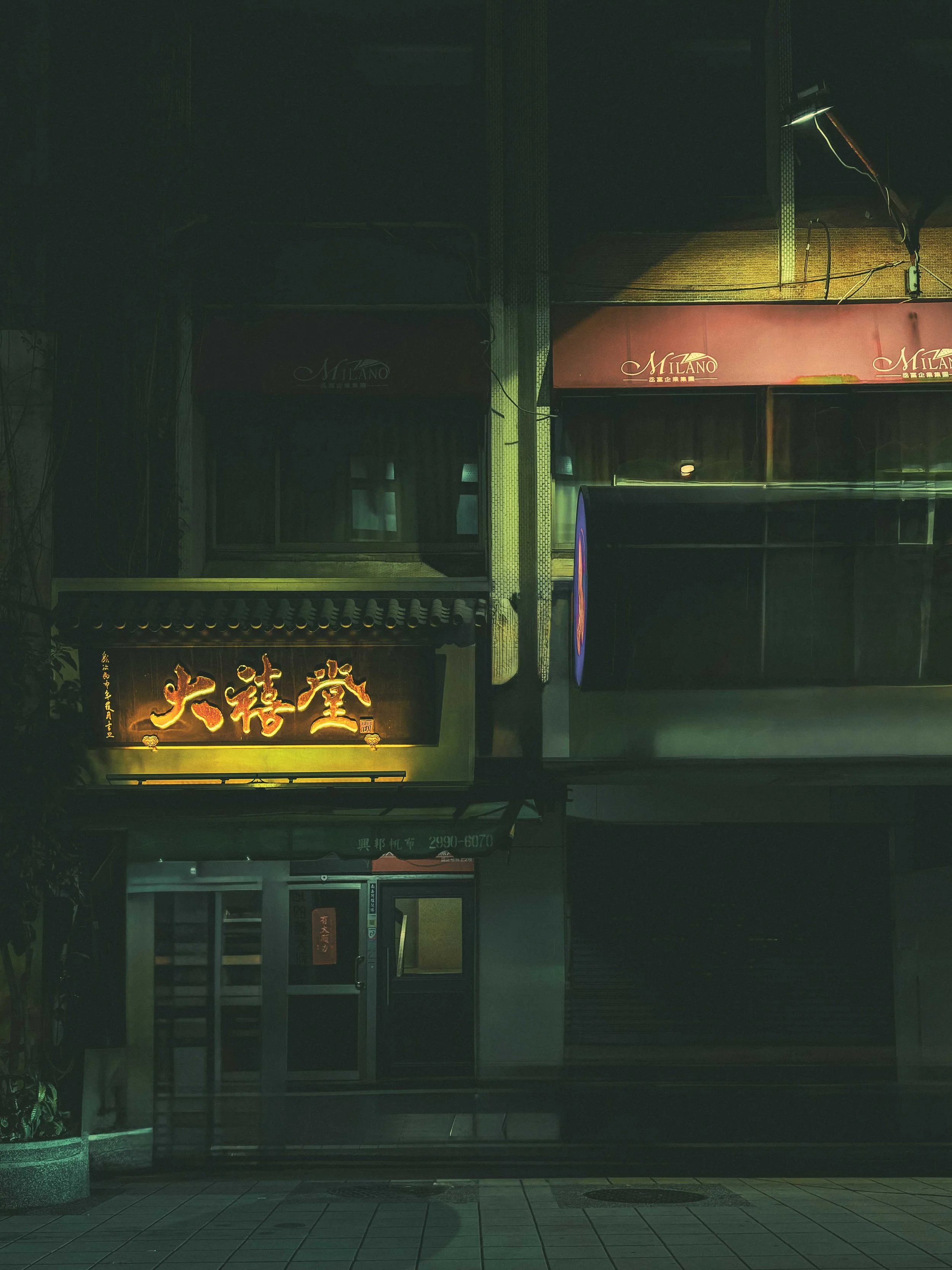 Nighttime scene of a closed storefront with Chinese characters illuminated on a sign, and minimal lighting on the building facade.