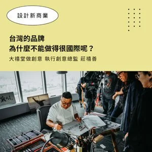 A man in a white shirt sitting at a desk with multiple television screens, using a desktop computer, in an office with large windows and a city view. Several people are standing around him, observing.