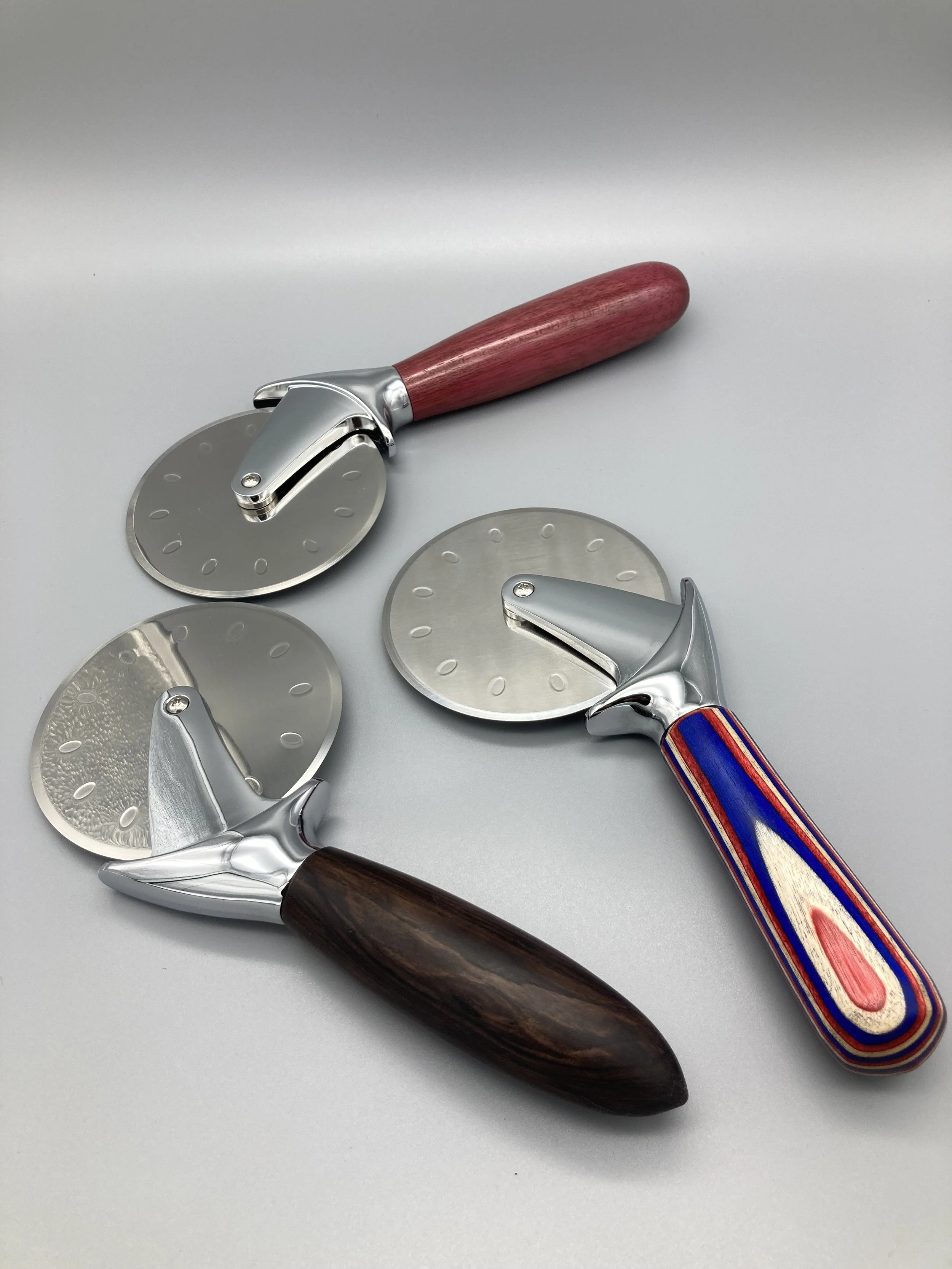 Three pizza cutters with different handles on a plain surface.