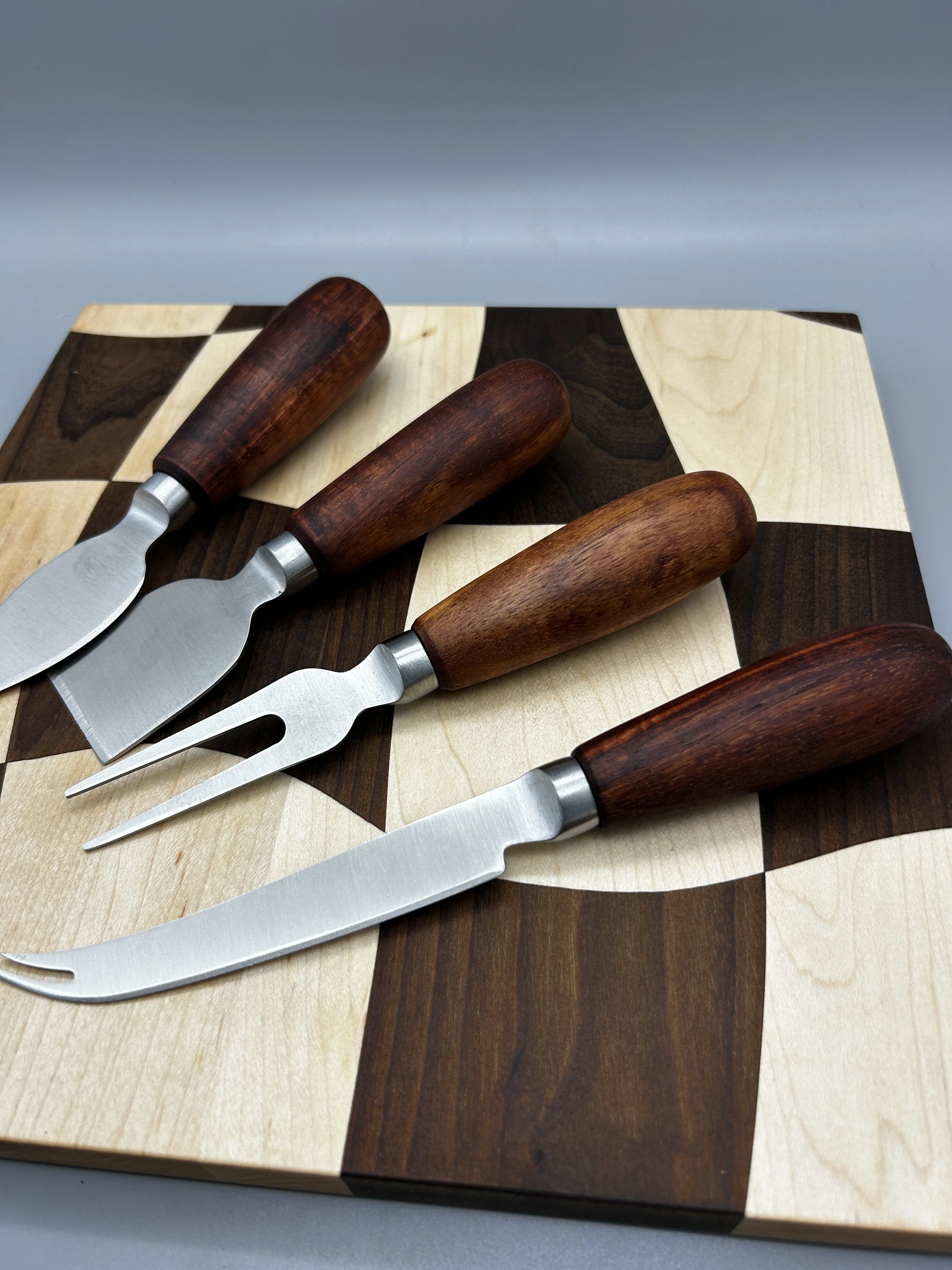 Four cheese knives with wooden handles are placed on a wooden chessboard.
