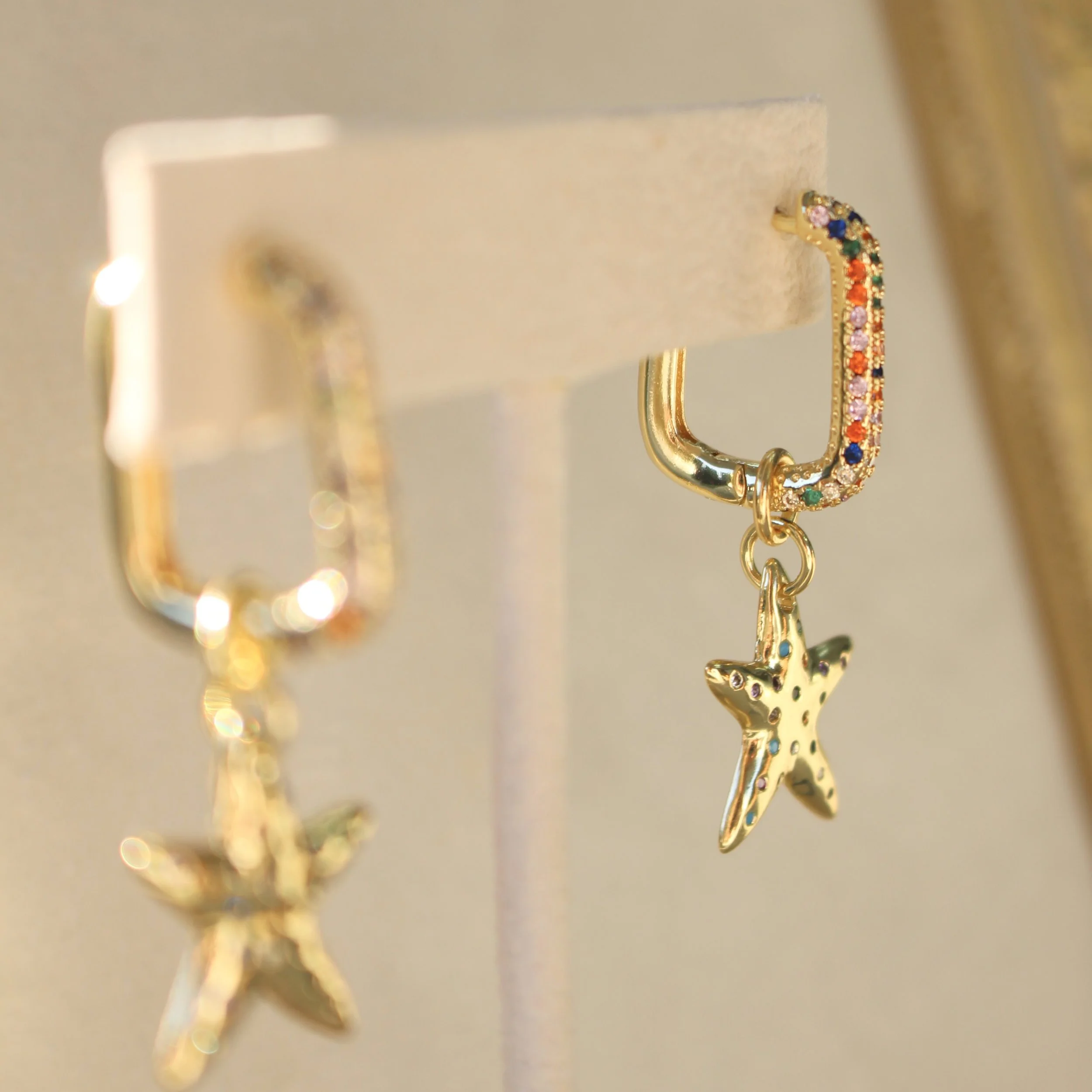 Gold hoop earrings with star charms, one featuring colorful gemstones and the other with small gemstone accents.