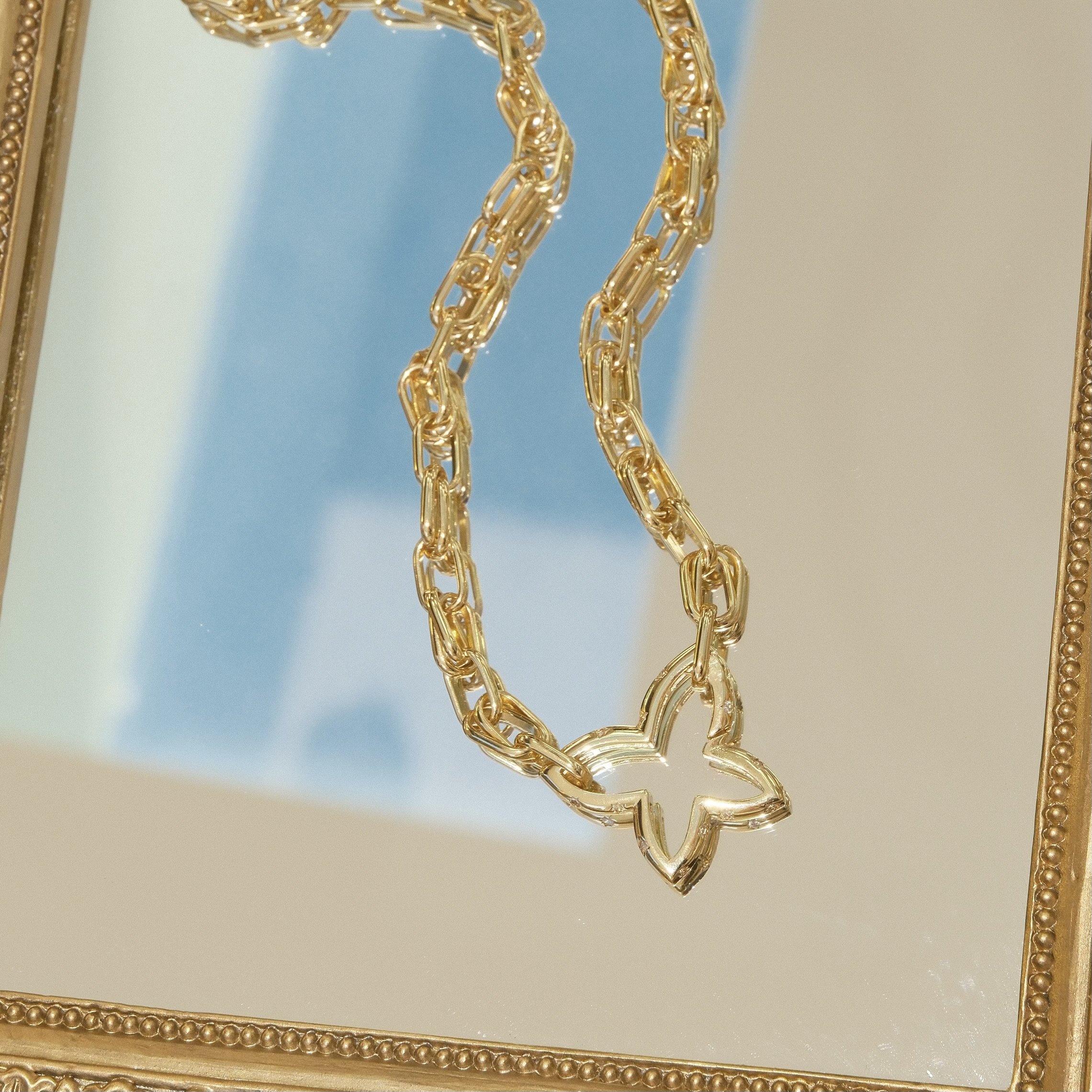 A gold chain necklace with a butterfly-shaped pendant hanging in front of a mirror.