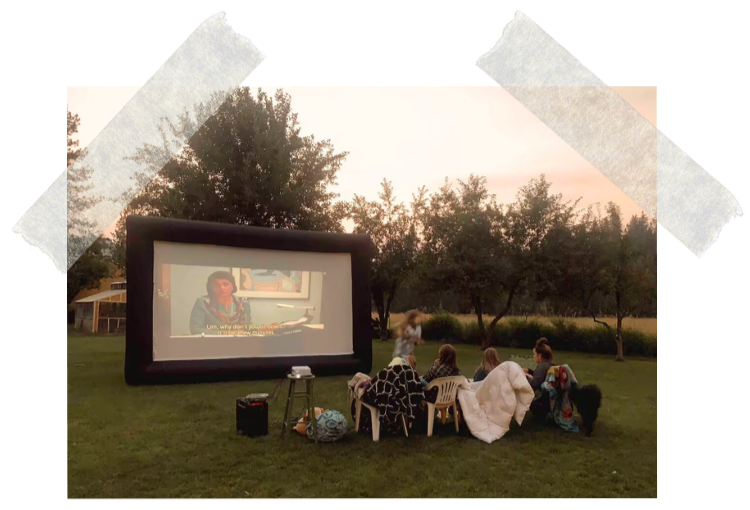 People sitting outdoors on chairs watching a movie projected on an inflatable screen in a backyard at dusk.