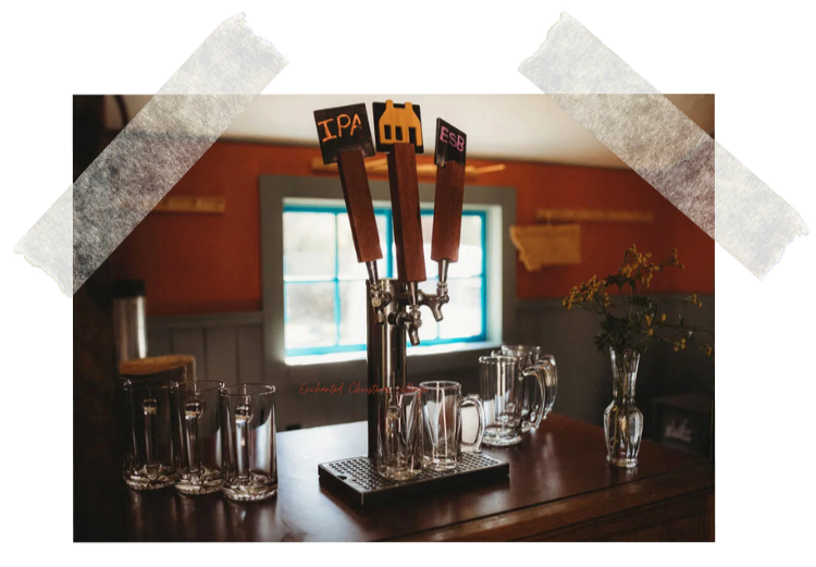 Yellow exterior wall of a building with a red mailbox, a black-framed window with red grid, a handmade sign reading 'the store' with red hearts, a rustic wooden door slightly open, a metal milk can, a long gray bench, and wood logs stacked underneath.