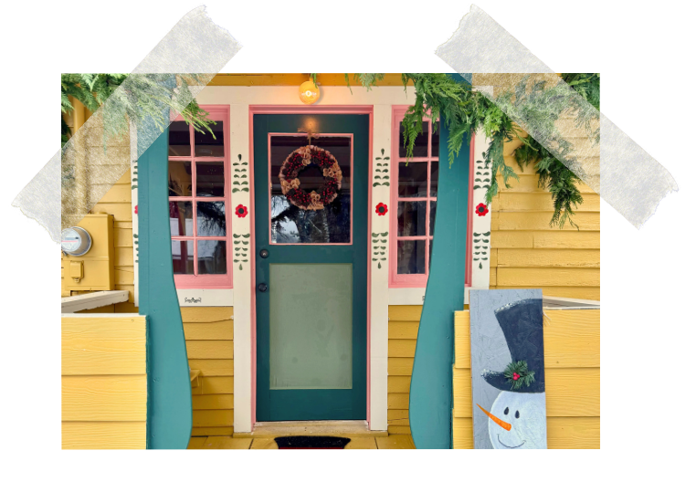 Front view of a yellow house with red trim, featuring two windows with pink frames and decorative flower patterns, a red door with a glass panel and a pink bottom panel, and red curtains on the sides.