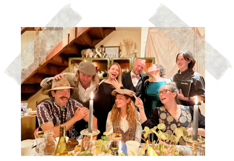 A group of ten people enjoying a celebration at a dinner table, some wearing vintage and costume hats, with candles and decorated table setting, in a cozy, warmly lit room with rustic décor.