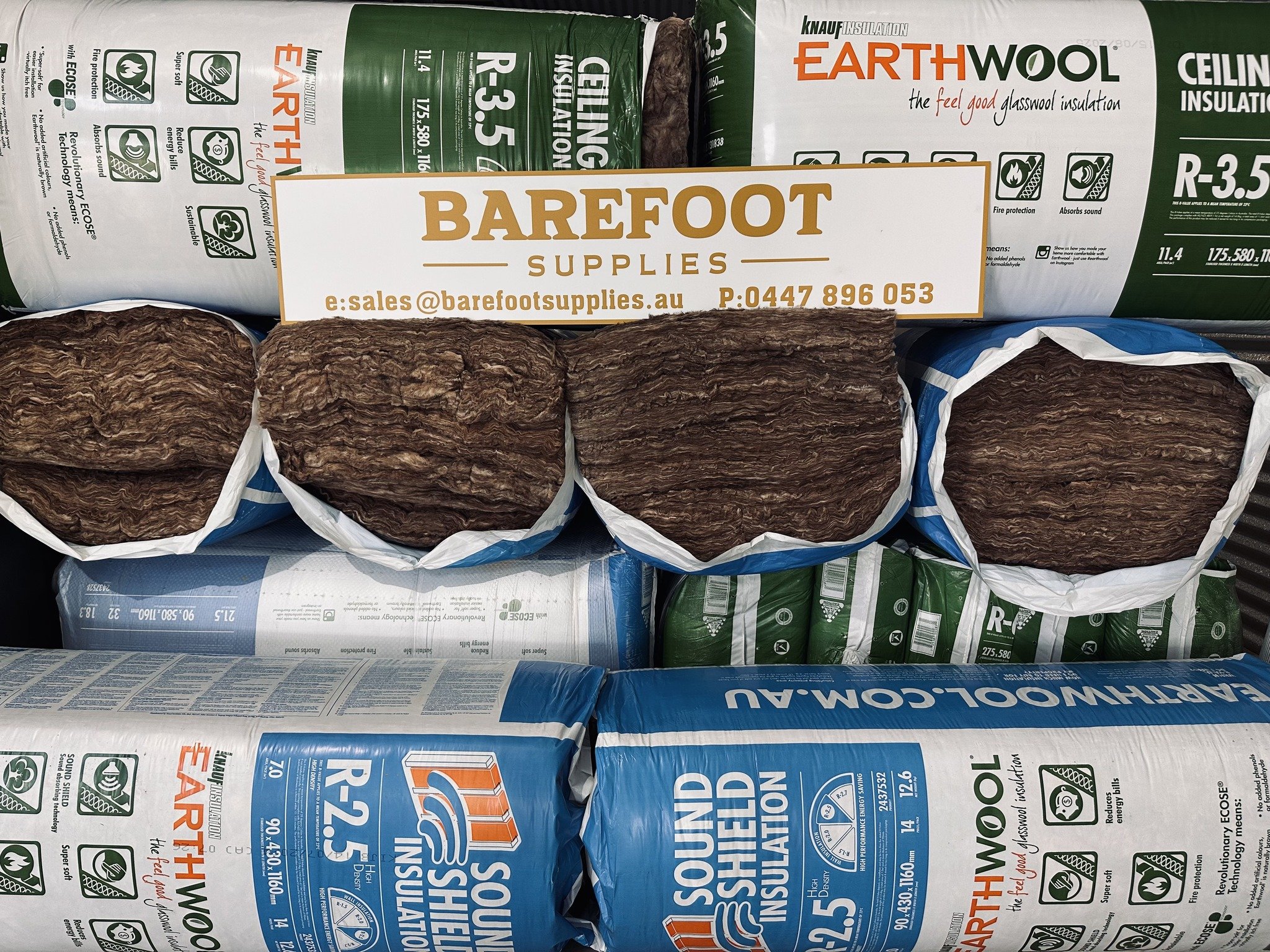 Bags of EarthWool insulation in front of a rolled-up insulation product, with a white sign labeled 'Barefoot Supplies' placed on top.