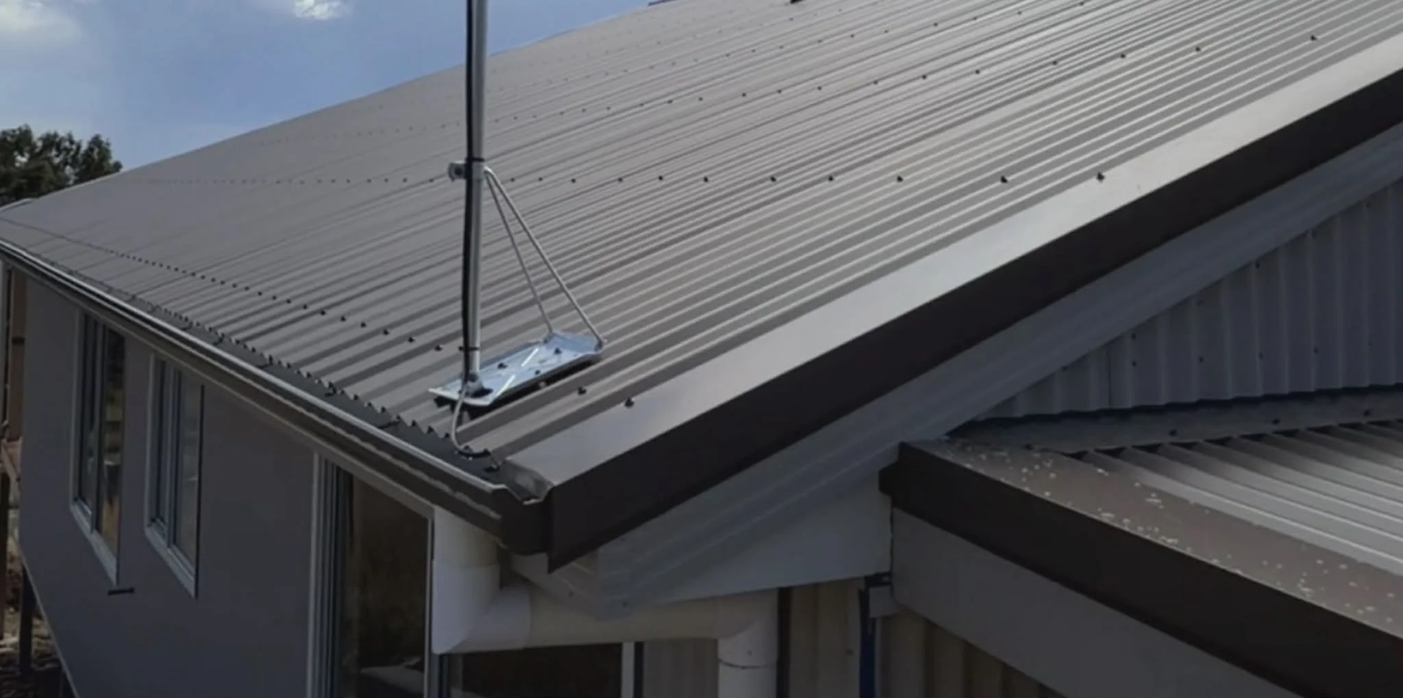 A close-up of a metal roof with a small antenna mounted on it, overlooking a windowed building, under a partly cloudy sky.