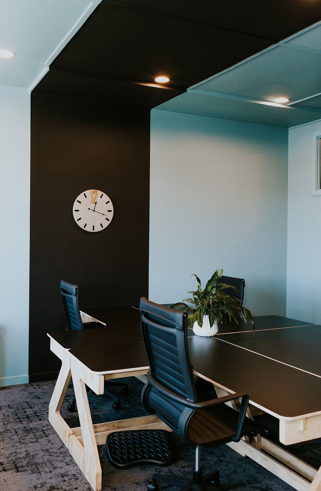 Modern shared office space with black desks, black chairs, a potted plant, and a wall clock showing 11:20.