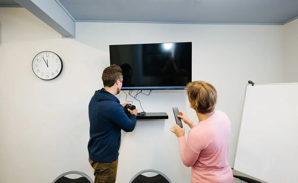 A man and a woman The Foundry meeting room in The Business Hive, demonstrating the use of a wall-mounted TV for video conferencing.