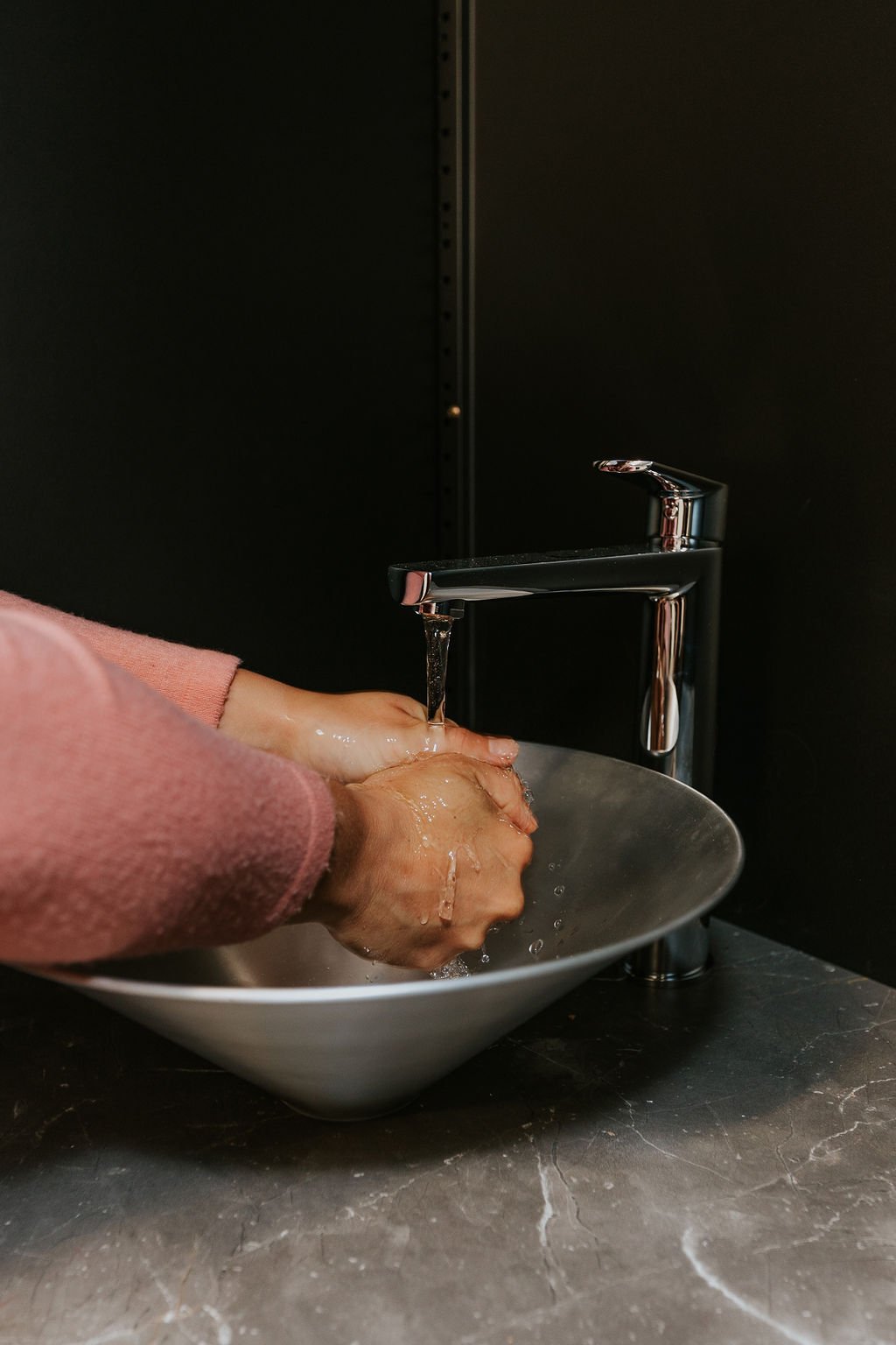 Person washing hands under running water from a modern faucet into a metal basin sink.