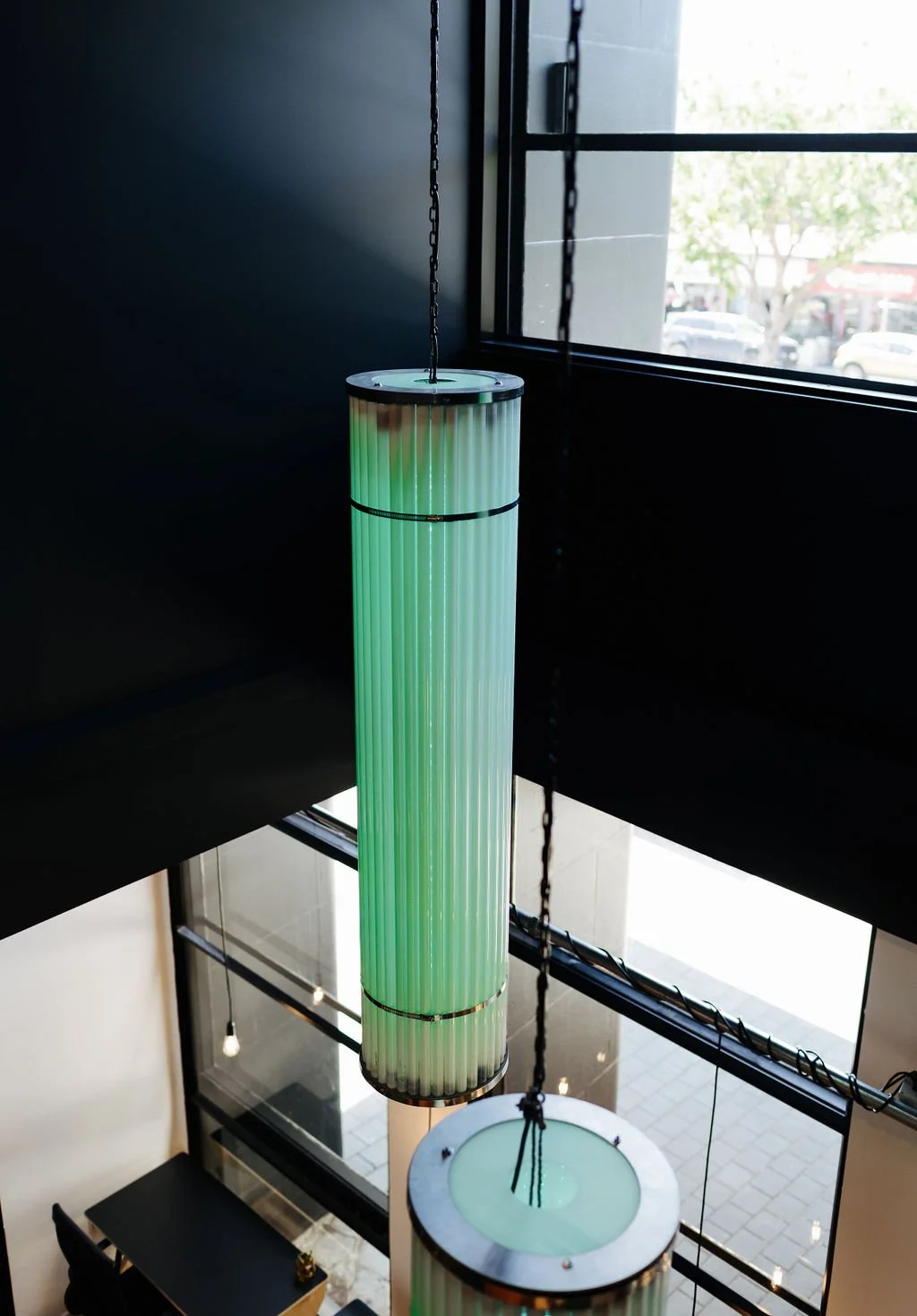 A green illuminated cylindrical pendant light hanging from a chain inside The Business Hive coworking space near a window.
