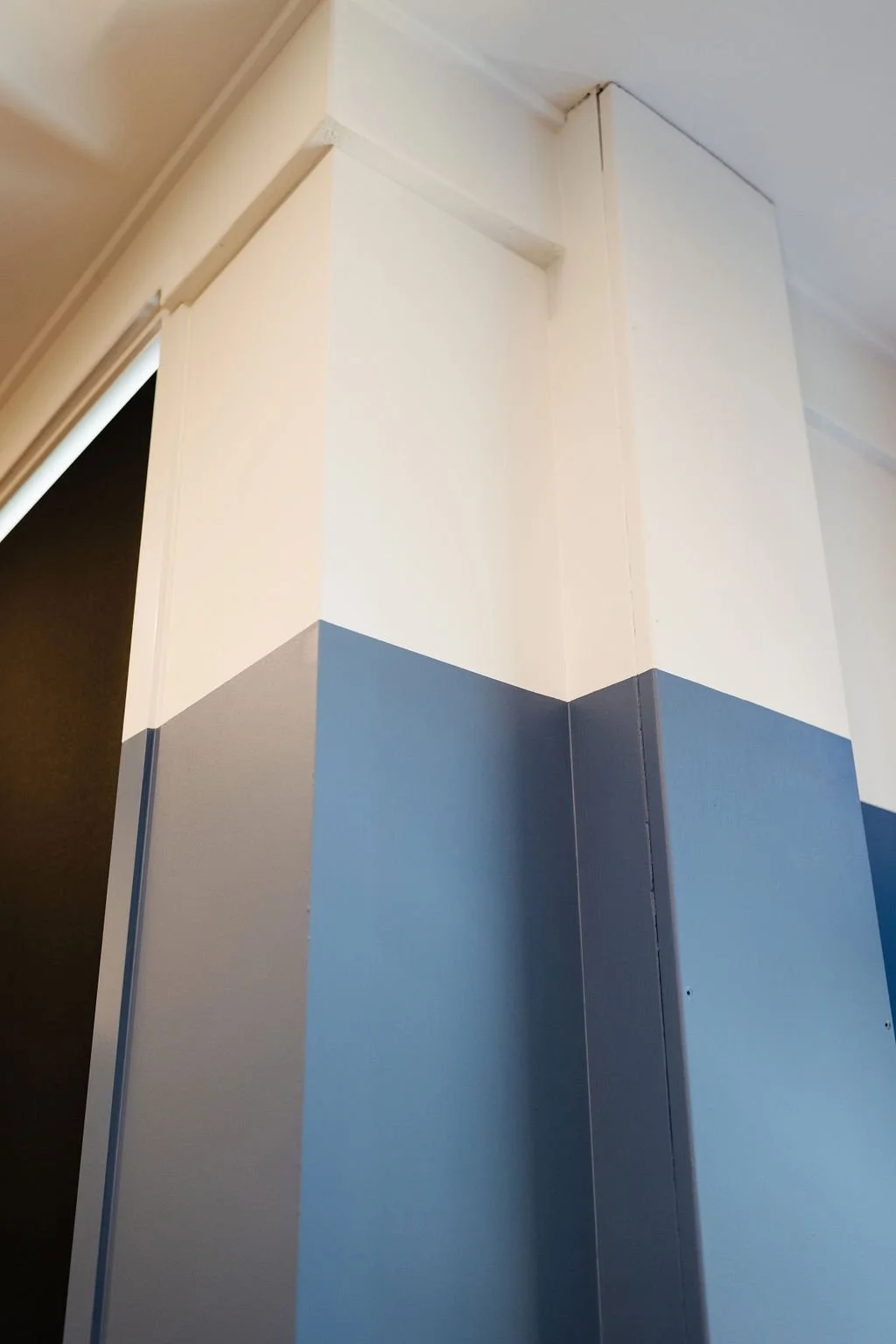 Close-up of a corner in an office with beige and blue painted walls, showing the intersection of ceiling, wall, and a doorframe.