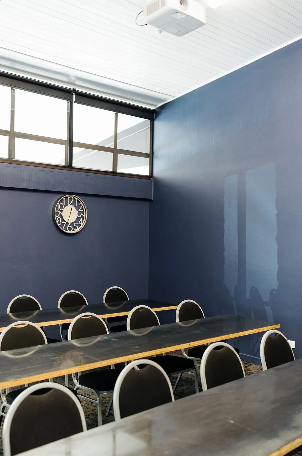 Empty conference room with blue walls, black chairs with metal rims, and tables, showing a wall clock above the chairs.
