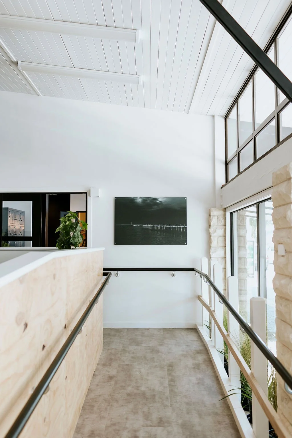 Wheelchair ramp in a modern interior with white walls, large windows, and a black and white landscape photograph.