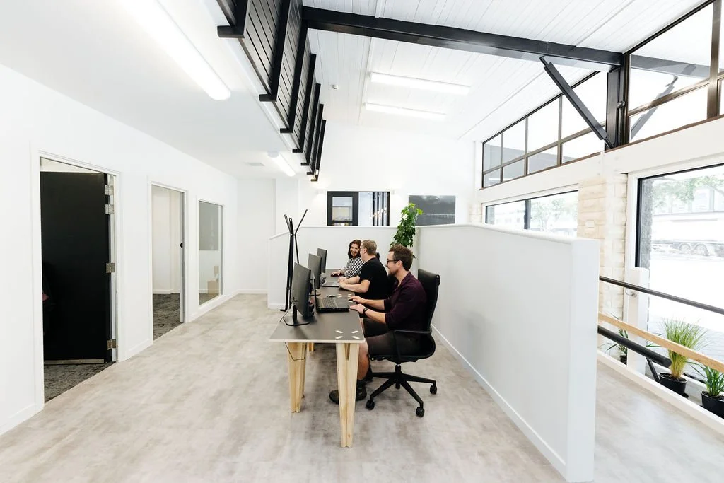 Three people working at computers in a bright, modern coworking space with large windows and high ceilings.