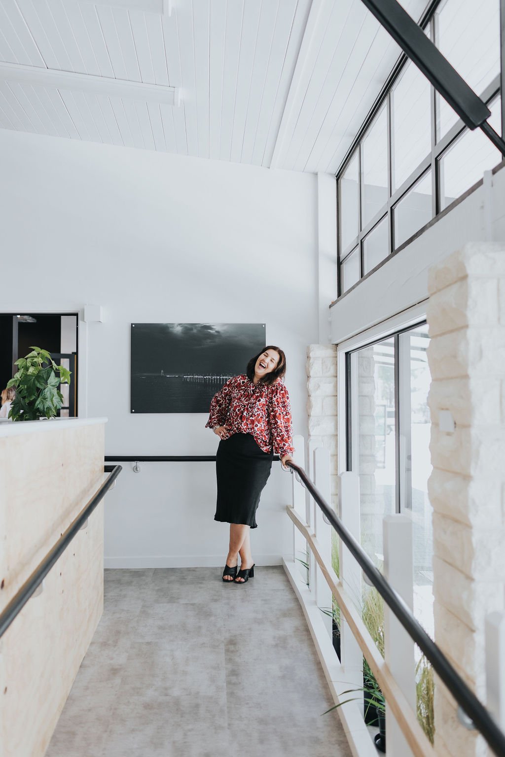 A woman laughing and standing at the top of a ramp inside The Business Hive coworking space with large windows and white walls.