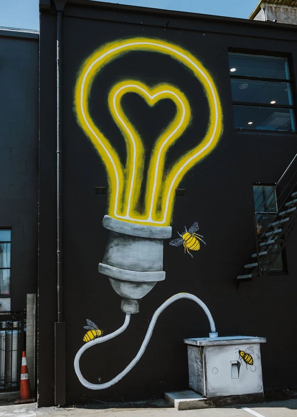Large mural painting of a lightbulb with two bees buzzing around it on the wall of The Business Hive coworking space