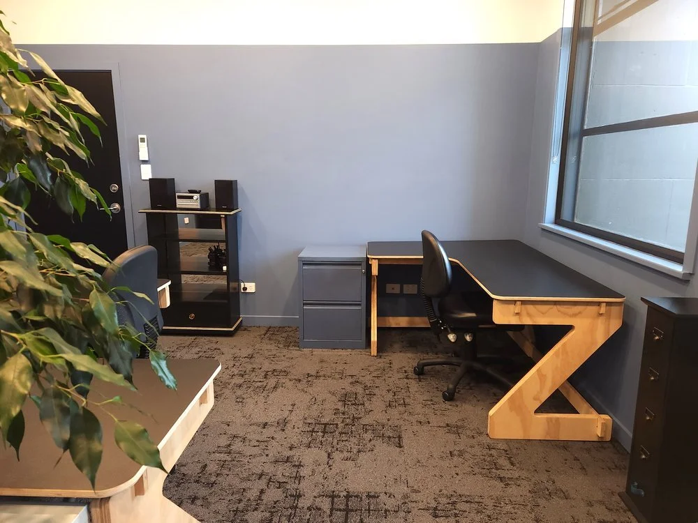 Blue and white private office Oamaru with black corner desks and a black door. There is a blue filing cabinet, a black glass-fronted cabinet with a stereo on top and a small black drawer set