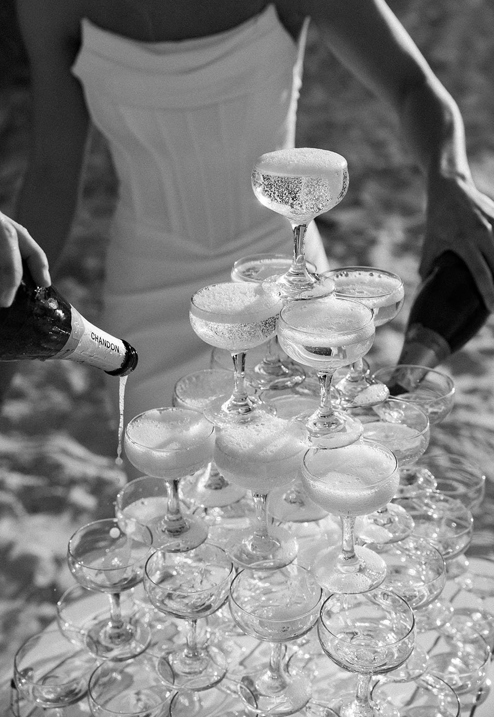 A person pouring Chandon champagne into a pyramid of champagne glasses.