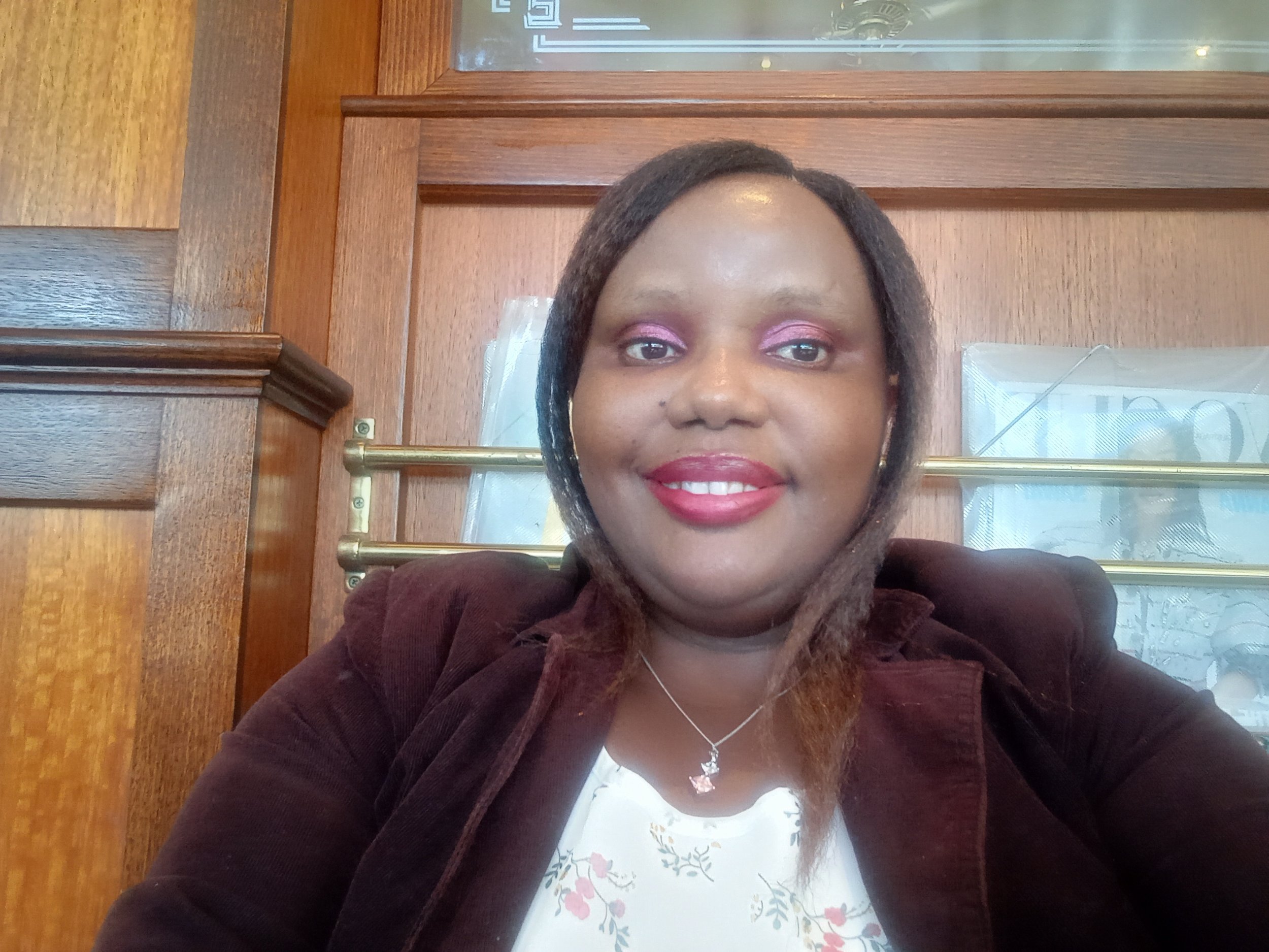 (Liz Angela Gaturu sitting in front of a wooden wall at a restaurant).