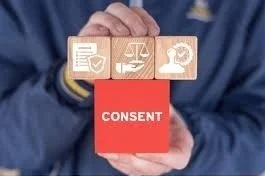 A person holding a card with icons representing documents, scales, a hand, and a globe. Below, there's a red block with the word 'CONSENT' in white letters.
