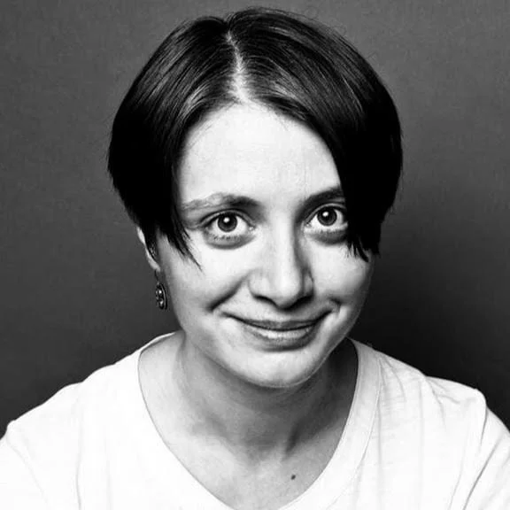 Black and white portrait of a woman with short dark hair, smiling slightly, wearing a light-colored top and earrings.
