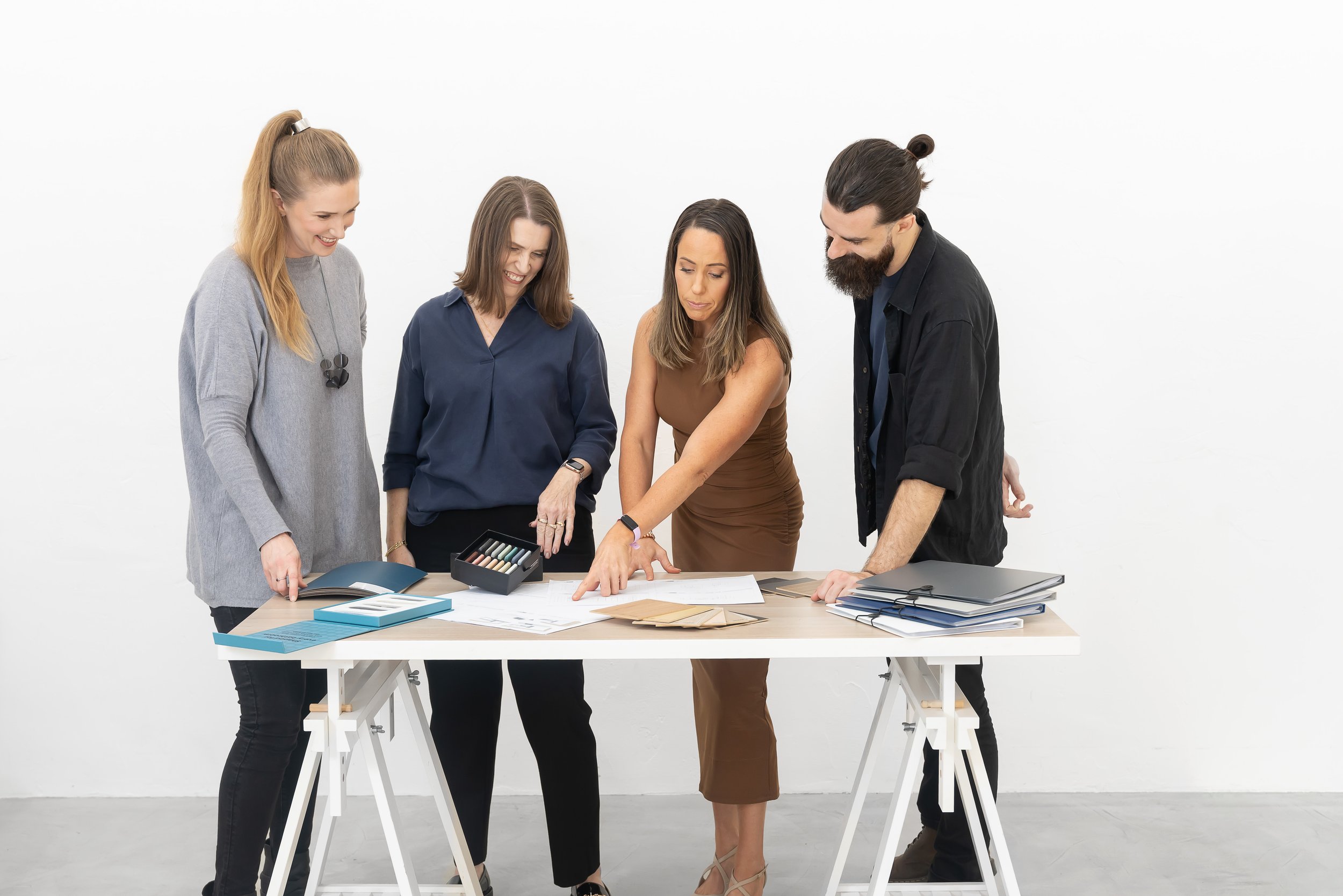 Four people looking at documents and samples on a white table in a bright room.