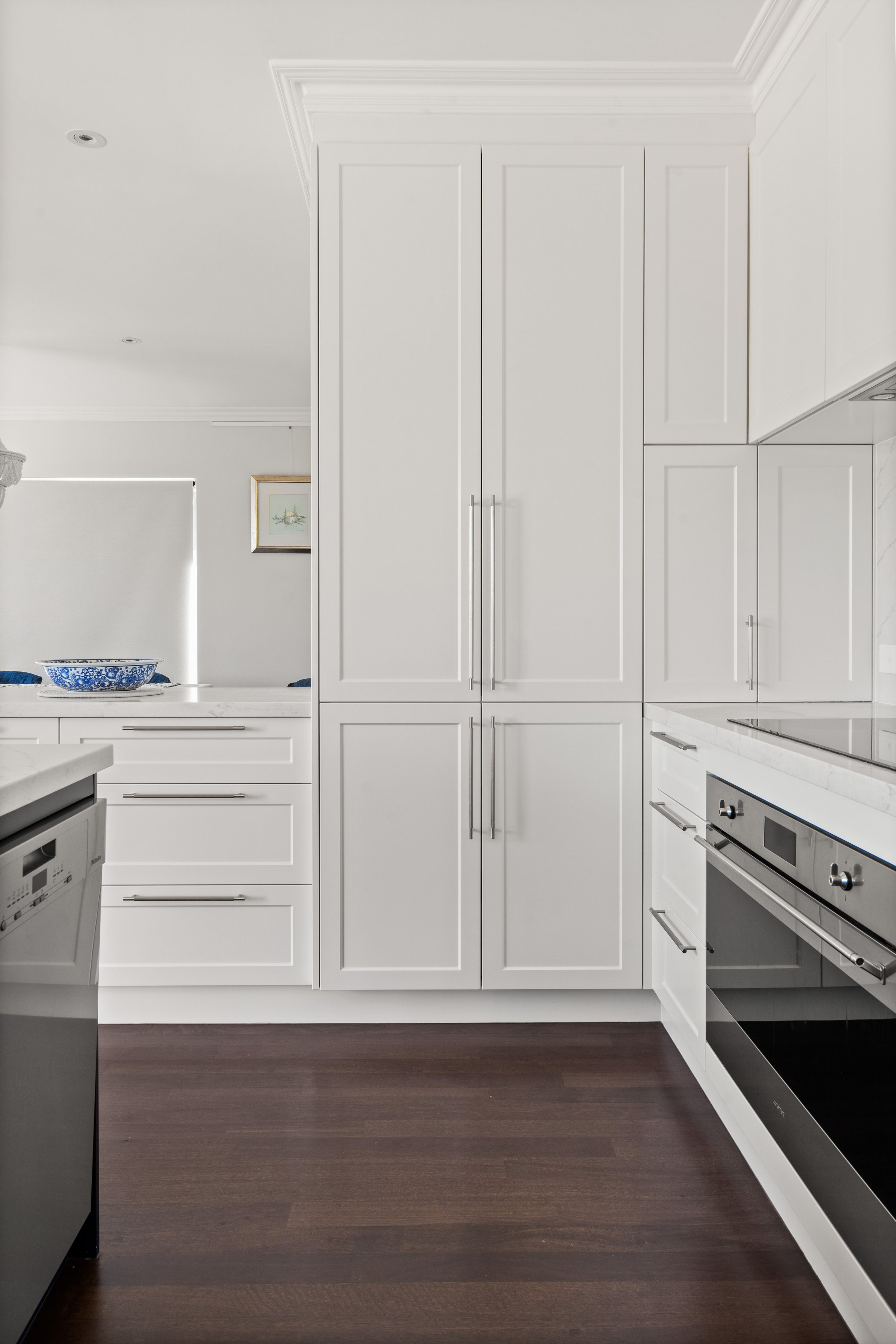 Modern kitchen with white cabinets, stainless steel appliances, and dark wood flooring.