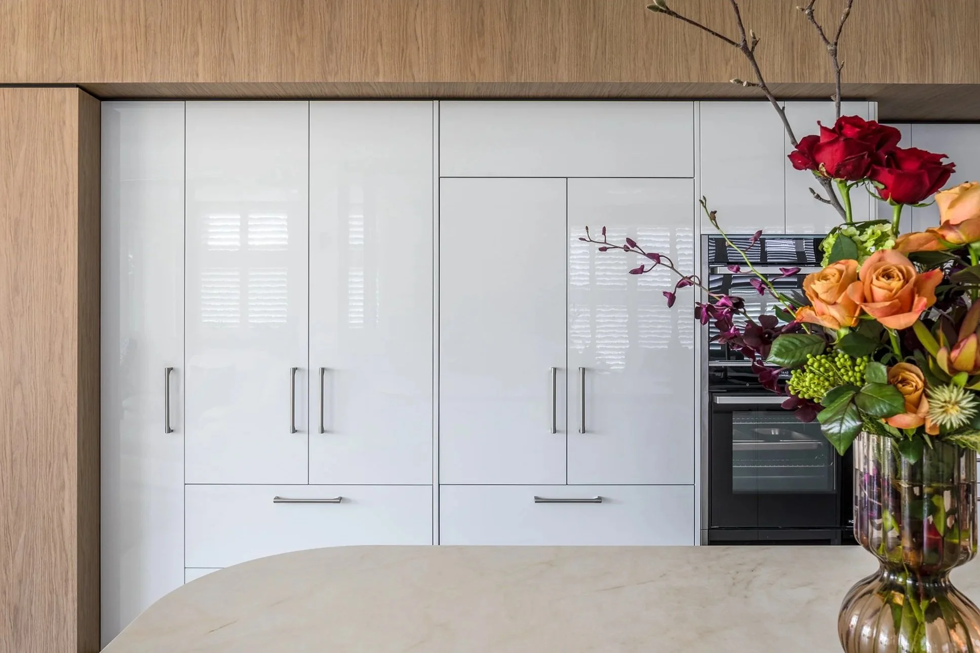 Close-up of a flower arrangement in a glass vase on a kitchen counter with white cabinets and wooden accents in the background.
