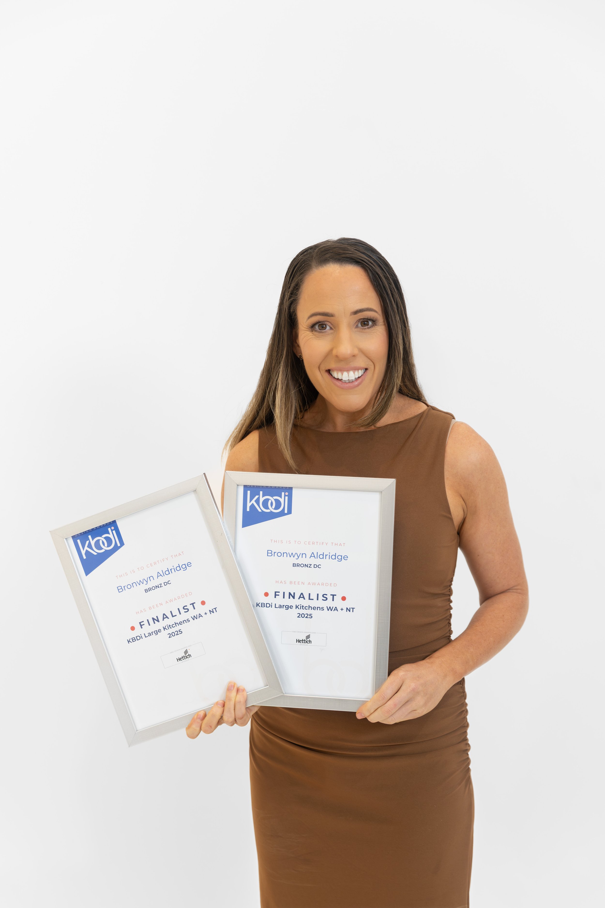 A woman holding two award certificates, smiling at the camera against a plain white background.
