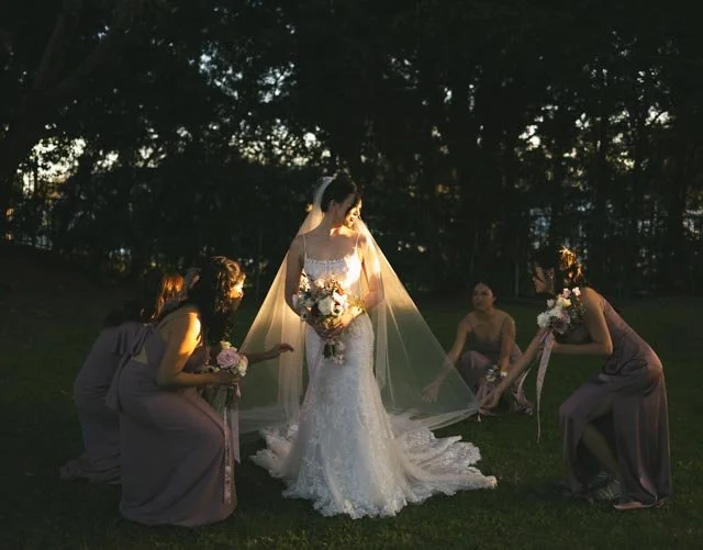 A bride in a white wedding dress holding a bouquet, surrounded by four bridesmaids in gray dresses holding bouquets, then posing outdoors during sunset with trees in the background.