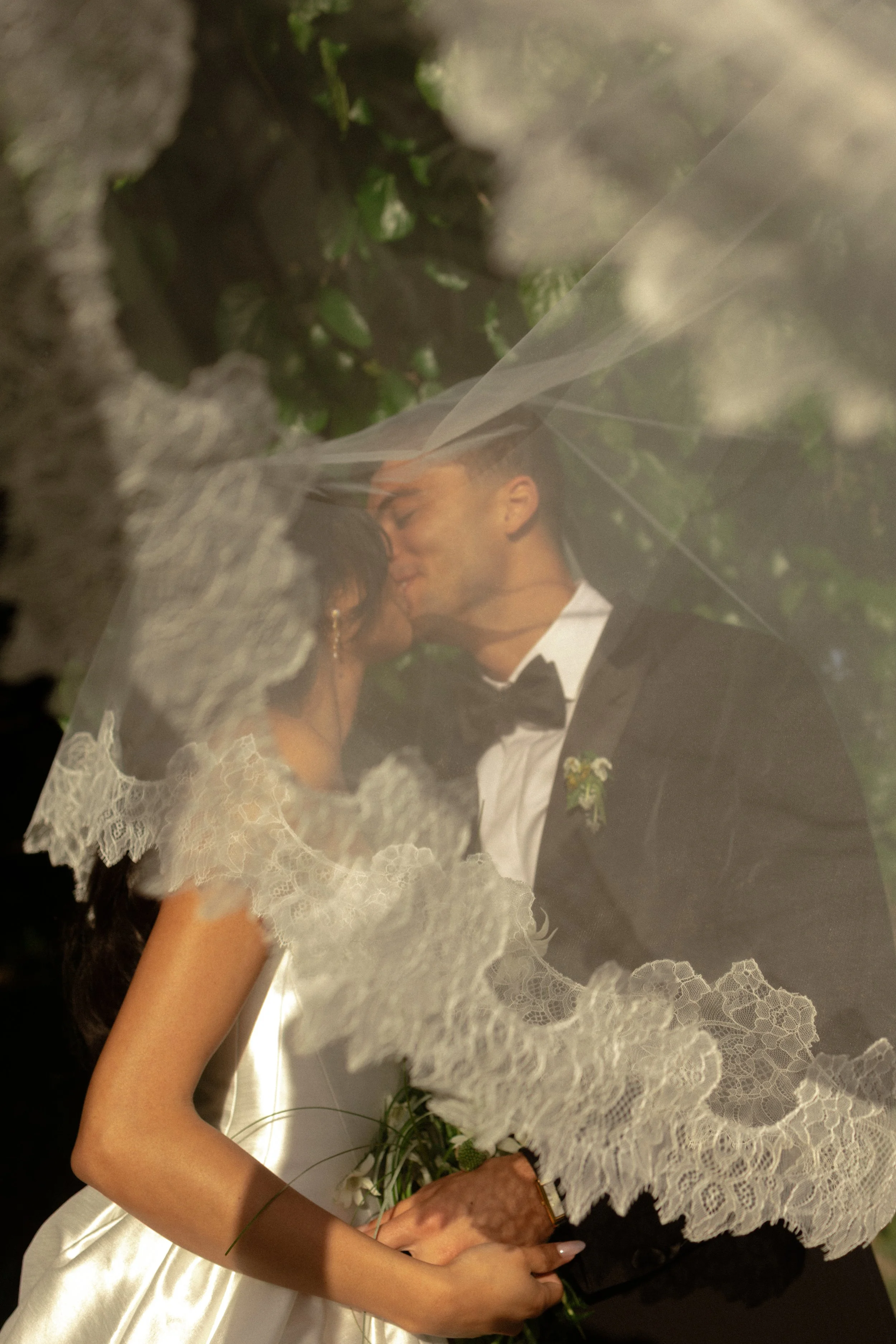 A newlywed couple sharing a kiss under a lace bridal veil during their wedding celebration.