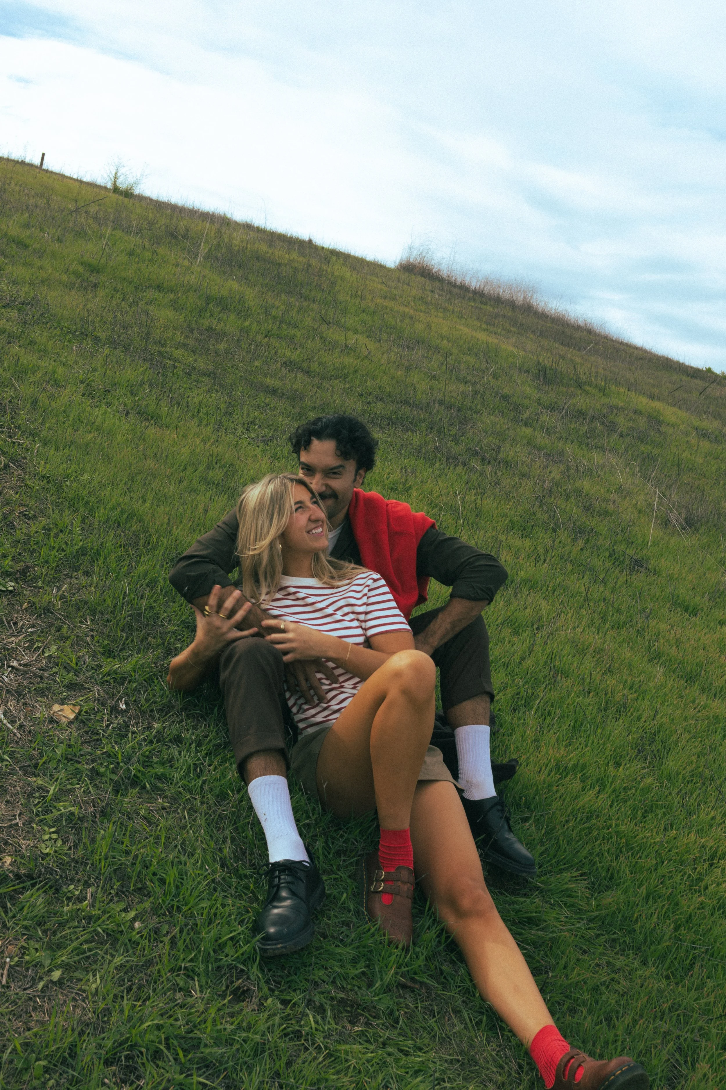 A young man and woman sitting on a grassy hillside, smiling and embracing each other. best wedding photographer in southern California 