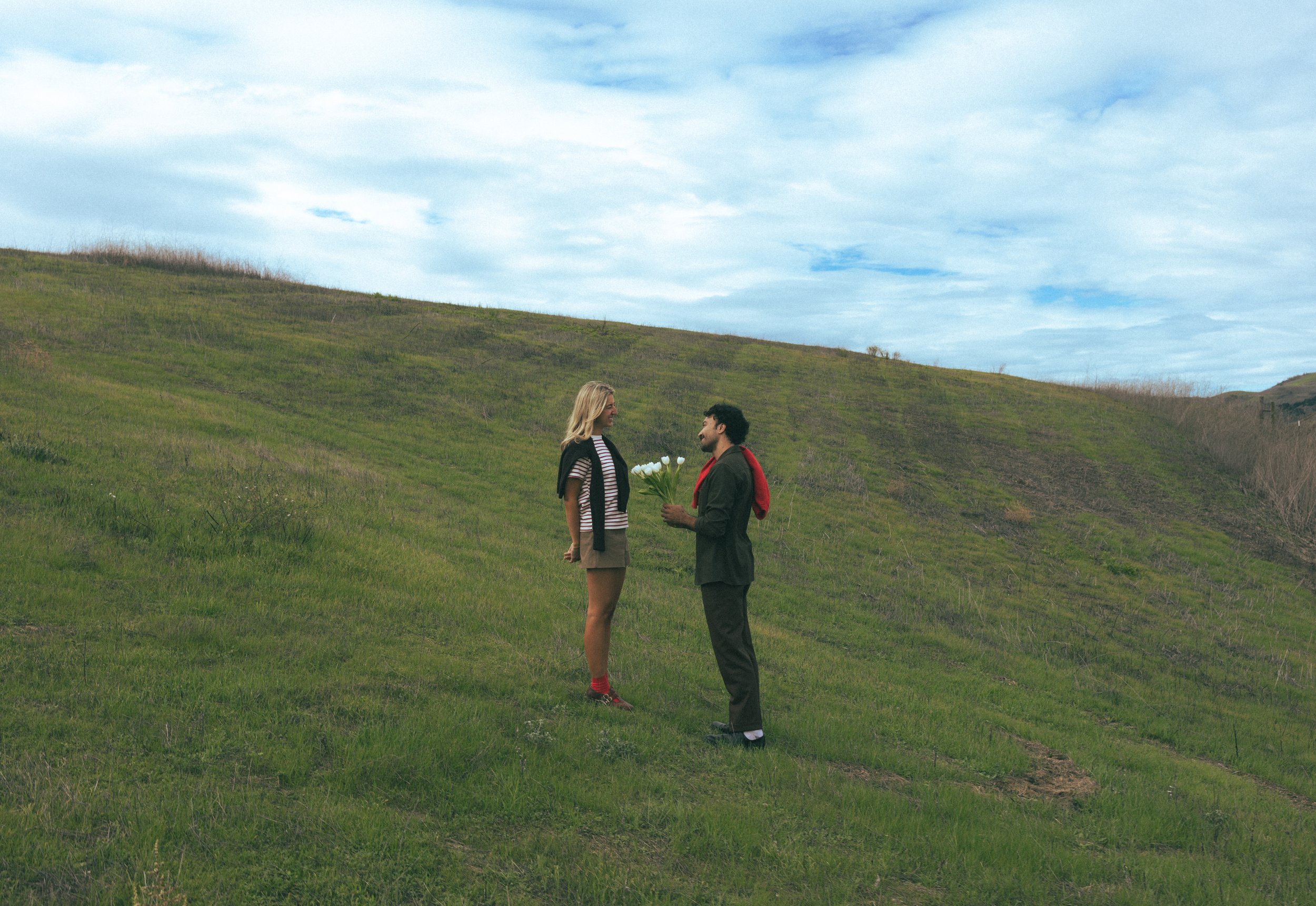 A man giving a woman flowers on a grassy hillside during daytime. best wedding photographer in Paris 