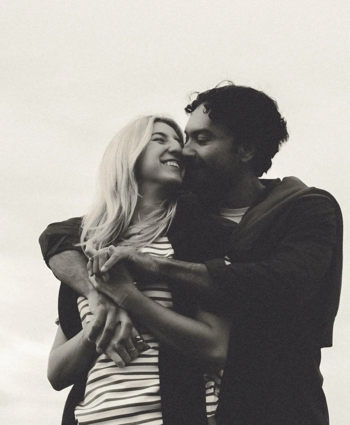 A black and white photo of a couple embracing closely, smiling and showing affection.