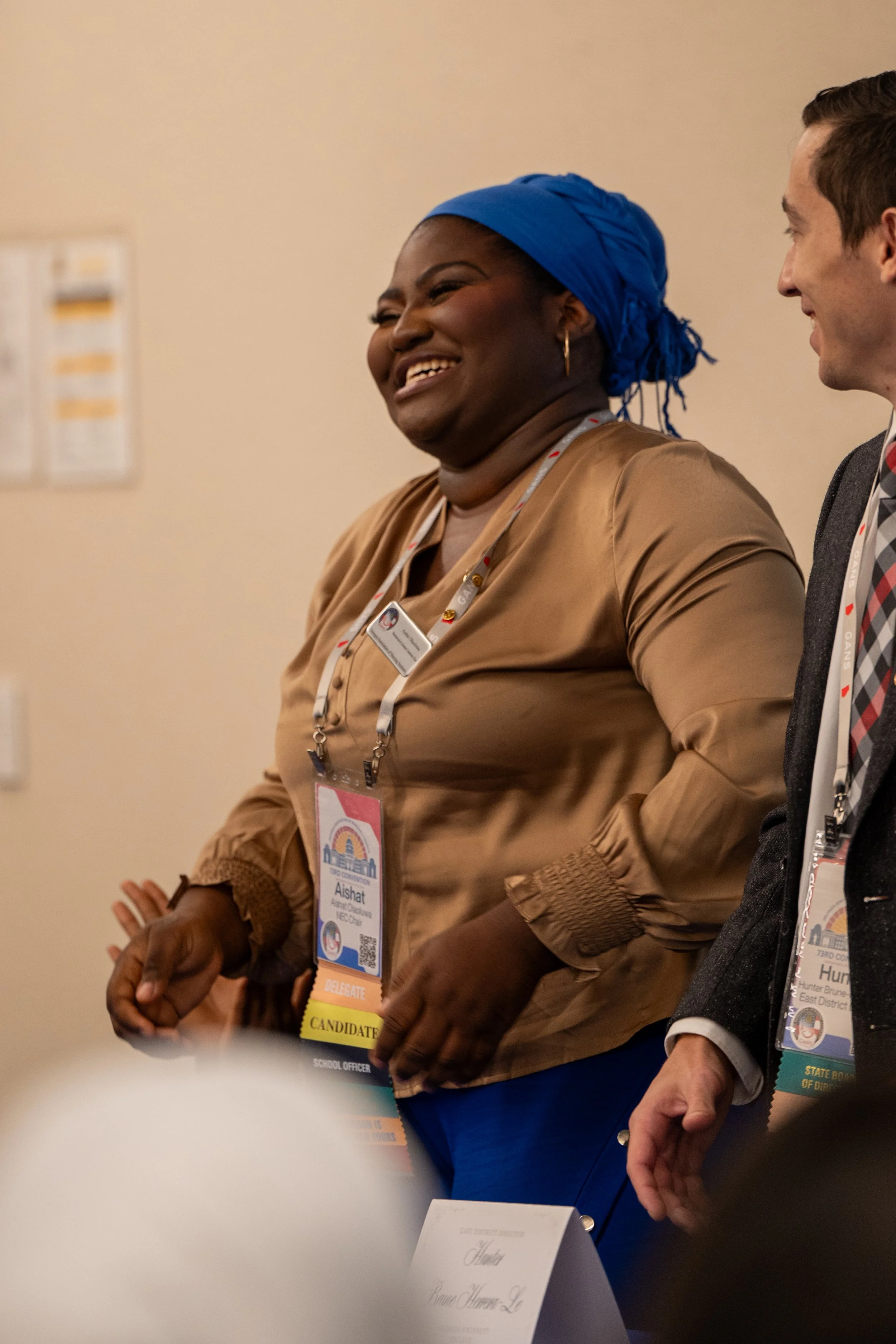 People wearing event badges, standing in a hallway, smiling, at a conference or convention.