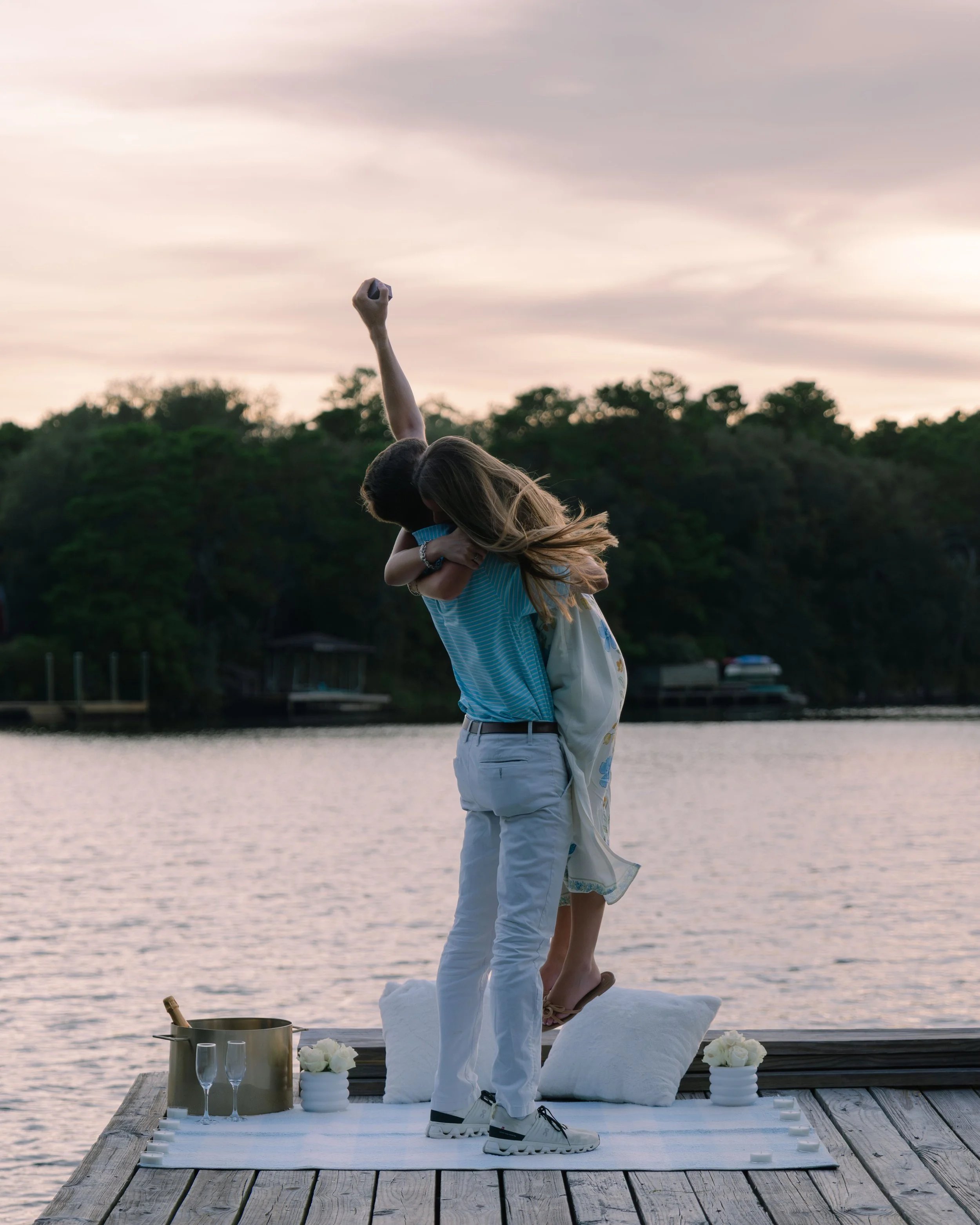 Young man lifting up woman with hand in the air in the sunset on a dock after engagement. 30A Engagement Photographer